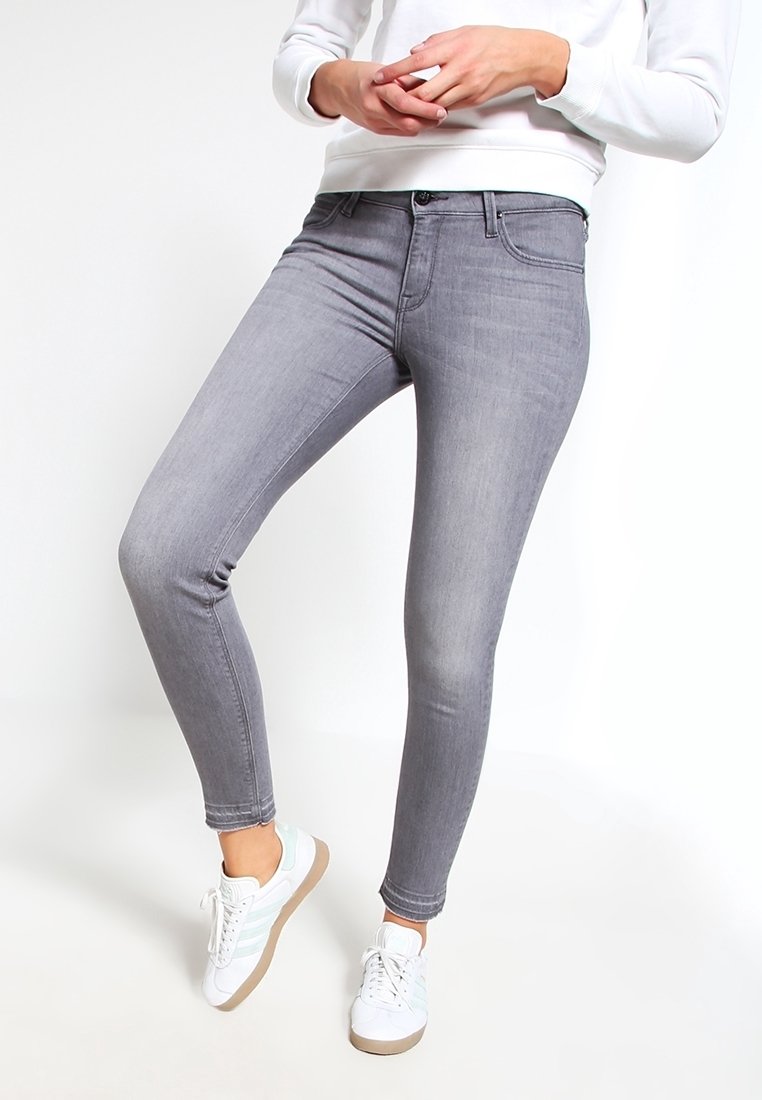 Vaqueros ajustados grises con una textura suave, que presentan cinco bolsillos, pasadores para cinturón y un ligero desgaste, combinados con zapatillas blancas.