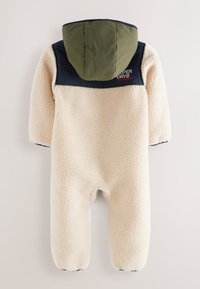 Krémový fleecový overal s zeleným a tmavomodrým golierom a kapucňou. Štruktúrovaný povrch; obsahuje logo v oblasti hrudníka.