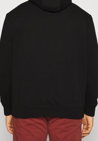 Svart huva tröja med en mjuk textur, med en avslappnad passform, ribbade manschetter och en rak fåll, ihop med burgundy-byxor.