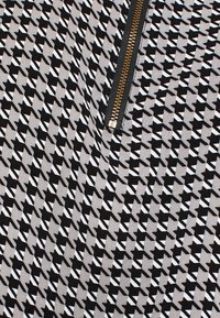 Schwarz-weißer Stoff mit geometrischen Mustern, mit einem sichtbaren Metallreißverschluss und einem goldenen Ziehgriff.