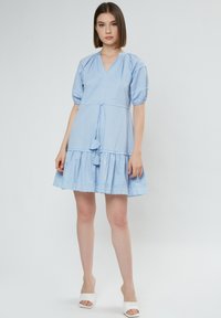 Hellblaues kurzes Kleid mit V-Ausschnitt, Puffärmeln und einem gestuften Rüschensaum, der am unteren Rand mit gewelltem Spitzenbesatz verziert ist.