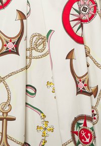 Tissu blanc avec un motif nautique comportant des ancres marron, des compas rouges et verts, des cordages et des accents décoratifs en or et rose.