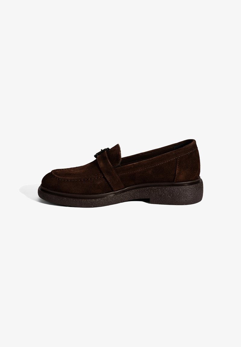 Mocassin en daim marron foncé avec semelle épaisse et détail de bride, vue de côté sur fond blanc.