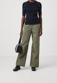 Tmavě modrý žebrovaný top s krátkým rukávem a knoflíkovými detaily; olivově zelené kalhoty s širokými nohavicemi; černá kabelka; černé boty. Jednoduchý a moderní design.