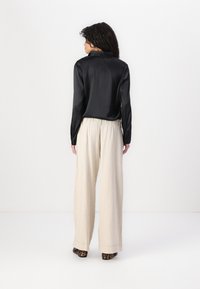 Chemise en satin noir avec un col, associée à un pantalon en lin beige clair décontracté. Des escarpins à imprimé animal complètent la tenue.