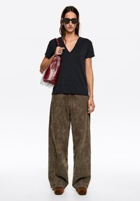 Czarny t-shirt z dekoltem w serek ozdobiony małymi srebrnymi kropkami, zestawiony z szerokimi brązowymi spodniami w wzory oraz czerwoną torbą z białą podstawą. Na nosie czarne okulary przeciwsłoneczne.