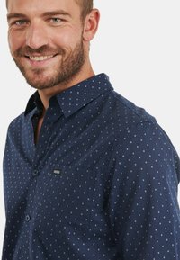 Camicia button-up blu navy con pois bianchi, maniche lunghe, colletto e taschino sul petto con etichetta del marchio. Materiale in cotone.