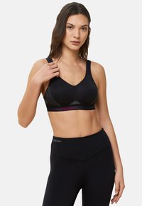 Zwarte sportbh met een geribbeld textuur, een V-halsontwerp, brede bandjes en een gemusterde band. Gecombineerd met hoge zwarte leggings.