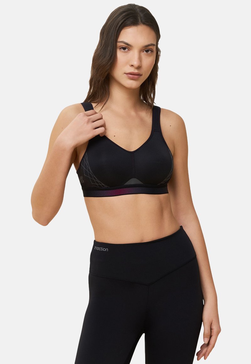 Zwarte sportbh met een geribbeld textuur, een V-halsontwerp, brede bandjes en een gemusterde band. Gecombineerd met hoge zwarte leggings.