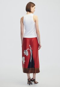 Rode satijnen rok met bloemmotief in wit en zwart. Heeft een gladde textuur en een bruine zoom. G gedragen met een strakke witte tanktop.
