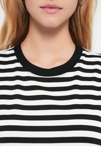 Μπλούζα με κοντά μανίκια, μαύρες και λευκές ρίγες, με ριμπ μαύρο γιακά, εμφανίζεται από το λαιμό και κάτω. Ομαλή υφή υφάσματος, χωρίς σχέδια ή μεταλλικά στοιχεία.