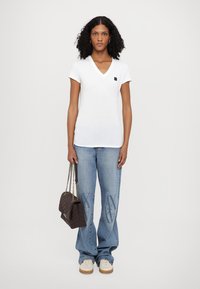 Camiseta blanca de cuello en V con mangas cortas, combinada con vaqueros de pierna ancha en azul claro con detalles estampados y un bolso acolchado oscuro.