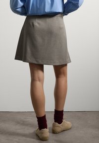 Falda gris hasta las rodillas con una textura suave y un patrón sutil, combinada con zapatos beige y calcetines burdeos. Camisa de rayas azules visible arriba.