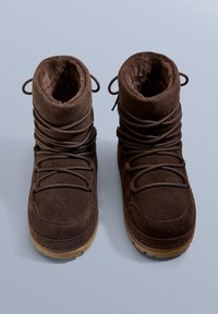 Brązowe botki zamszowe z miękką futrzaną wyściółką, z zaokrąglonym noskiem i ciasno sznurowanym wzorem, osadzone na teksturowanej gumowej podeszwie.