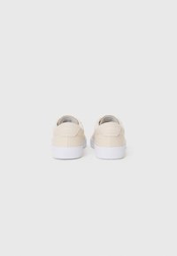 Sko med en glat beige overdel og hvid gummisål, der har en rund form og et subtilt logo på hælen.