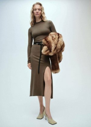Robe ajustée vert olive avec une fente sur le côté, ceinturée à la taille, associée à un châle en fourrure brune duveteux et des chaussures à talons hauts crème.