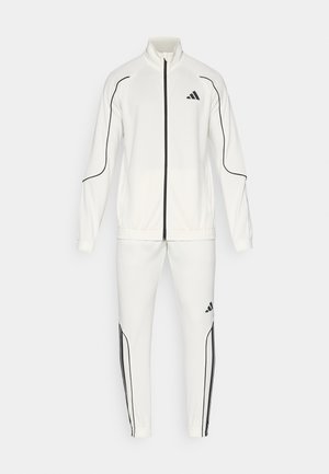 Witte trainingsoutfit bestaande uit een ritssluitingjack met hoge kraag en zwarte accenten aan de zijkanten, gecombineerd met bijpassende tapered broek, beide gemaakt van een soepele stof.