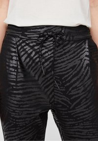 Czarne spodnie z połyskującym, teksturowanym wzorem w zebry. Posiadają elastyczny pas ze sznurkiem oraz gładki, elegancki materiał.