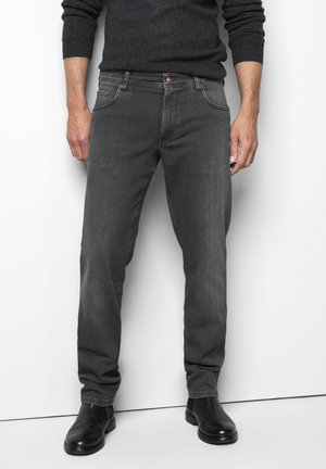Mann trägt dunkelgraue Slim-Fit-Jeans, schwarze Lederstiefel und einen dunkelgrauen Langarm-Pullover und steht vor einem weißen Hintergrund.