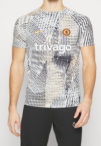 Short-sleeved Nike t-shirt with a white, black, and beige geometric pattern, featuring a Chelsea FC logo and "trivago" text in bold white.
