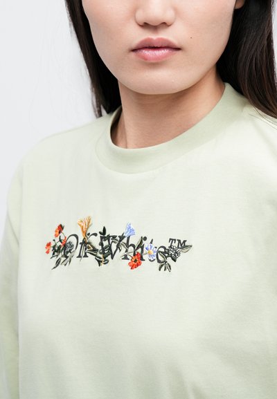 Vaaleanvihreä collegepaita pyöreällä kaula-aukolla, jossa on moniväristä kukka-embroiderya rinnassa, mukaan lukien punaista, sinistä ja keltaista.