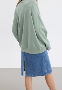 Groene sweatshirt met een relaxed fit en geribbelde zoom, gecombineerd met een denimrok met een zijsplit en een rafelige zoom.