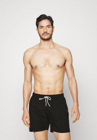 Shorts de bain noirs avec une taille élastique et un cordon de serrage, présentant une texture lisse et un design minimaliste. Aucun motif ou accent visible.