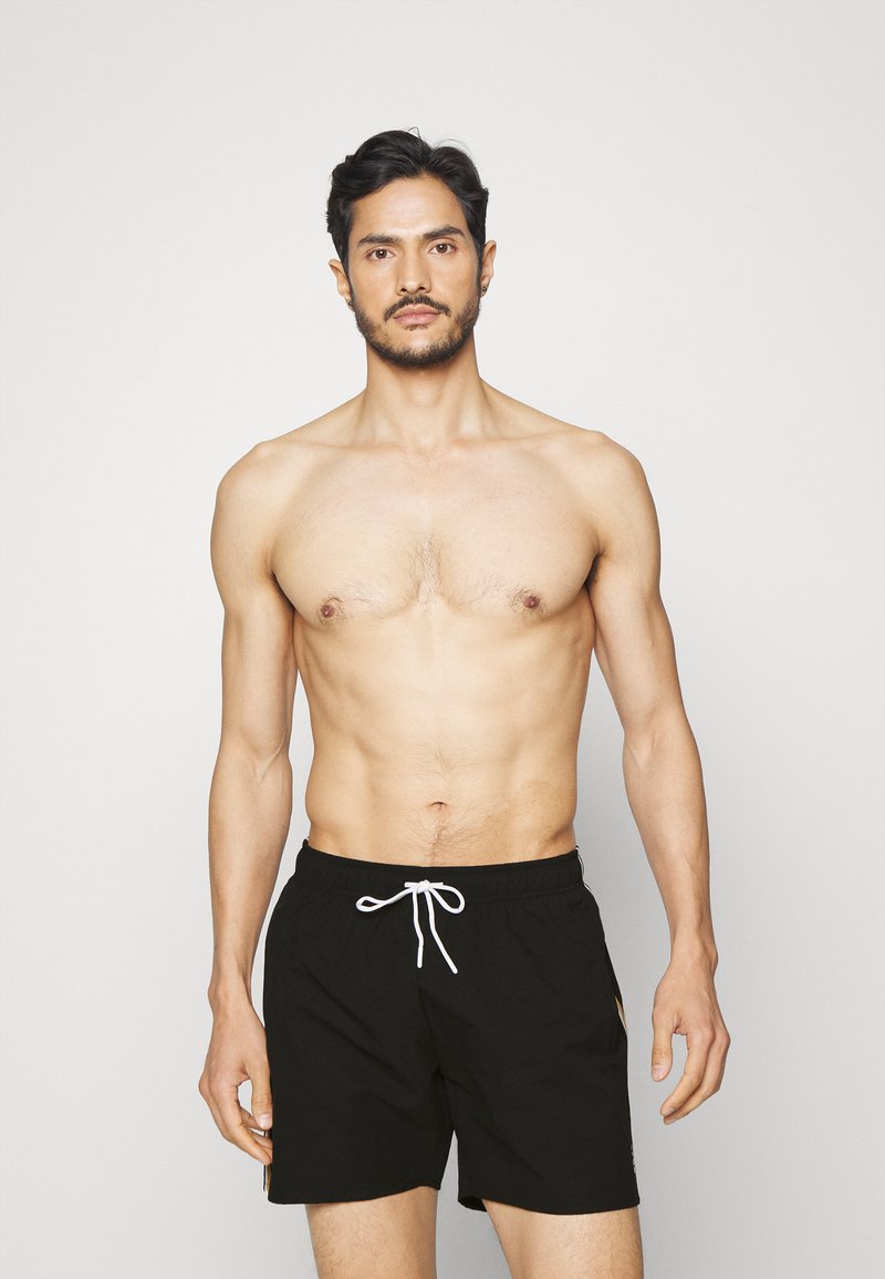 Shorts de bain noirs avec une taille élastique et un cordon de serrage, présentant une texture lisse et un design minimaliste. Aucun motif ou accent visible.