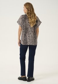 Top corto a maniche corte e vestibilità comoda, caratterizzato da una stampa leopardata in marrone e nero su uno sfondo beige, abbinato a pantaloni blu scuro su misura e scarpe nere.