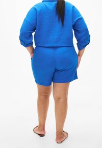 Set in lino blu composto da due pezzi, caratterizzato da una camicia corta con maniche arrotolate e pantaloni shorts coordinati, che mette in mostra un tessuto testurizzato e una vestibilità rilassata.