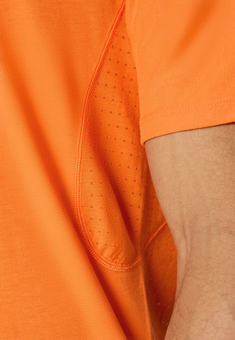 Camiseta de manga corta en tejido naranja brillante con un detalle de panel de malla en el costado, con textura suave y costuras en contraste.