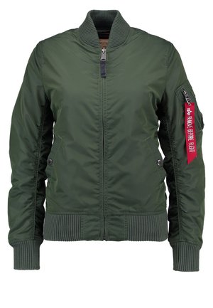 Giacca bomber verde oliva con colletto e polsini a costine, chiusura con zip frontale, tasche laterali e un etichetta rossa con la scritta "RIMUOVERE PRIMA DEL VOLO."