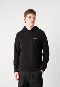 Svart hettegenser med framlomme, ribbede mansjetter og kant. Har en liten hvit Calvin Klein-logo på brystet. Myk stoffkvalitet.