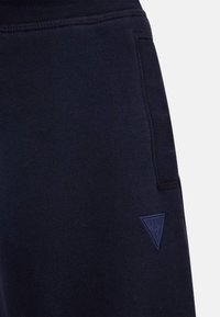 Navyblaue Sweatpants aus weichem Material mit einer strukturierten Oberfläche und einem kleinen, eingeprägten dreieckigen Logo auf der linken vorderen Tasche.