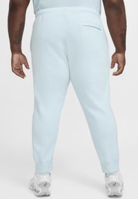 Joggers azul claro con un diseño ajustado, cintura elástica y detalle de bolsillo trasero, combinados con zapatillas deportivas blancas.