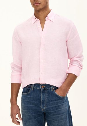 Light pink linen button-up shirt with long sleeves, worn with blue denim jeans. Features white buttons and a casual style.