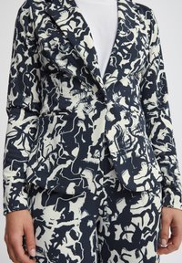 Navy and cream patterned blazer with a fitted design, featuring a single button closure and peak lapels.  Smooth fabric texture with abstract motifs.