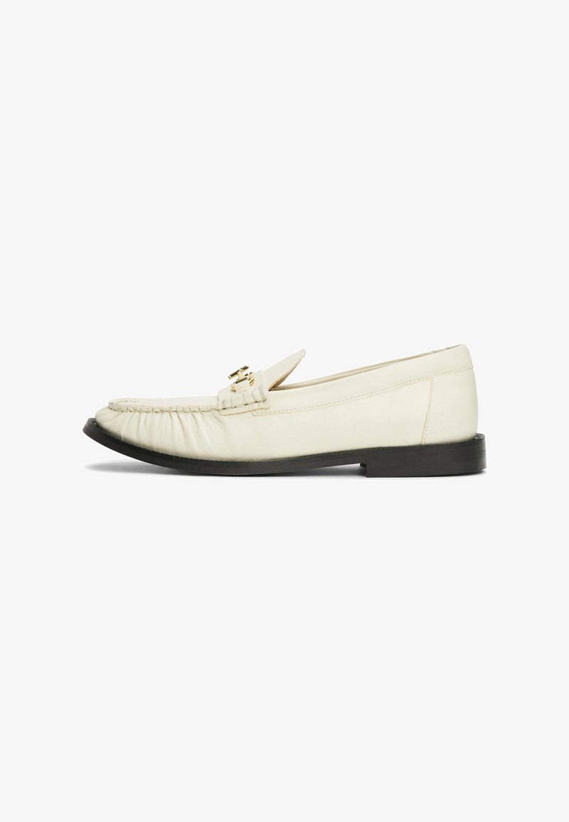 Cremefarbene Lederloafers mit abgerundeter Zehe, ausgestattet mit einer dekorativen goldfarbigen Schnalle und Raffung vorne, auf einer schwarzen Sohle.