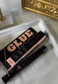 Tubo di eyeliner nero con finitura lucida, insieme a una scatola di colla per ciglia rosa e nera etichettata "COLLA" e "MELODY LASHES".