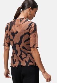 T-shirt marron transparent avec un motif abstrait noir, manches courtes à bords festonnés et encolure arrondie. Texture douce, tissu léger.