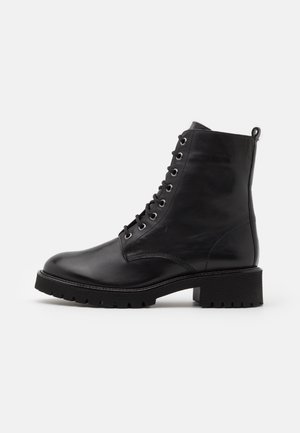 Sort læder ankelstøvle med snørebånd, chunky hæl og grovmønstret sål, set fra siden på ensfarvet hvid baggrund.