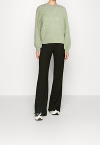 Ljusgrön texturerad tröja med lång ärm, i kombination med svarta utsvängda byxor. Modellen bär vita och svarta sneakers. Enkelt, avslappnat outfit.