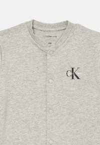 Svetlý šedý bavlnený žerzejový kardigán s výstrihom do V, zapínaním na päť gombíkov a potlačou loga "Calvin Klein". Mäkká textúra a ležérny dizajn.