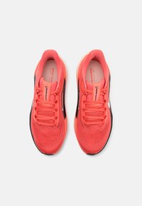 Nike tenisice za trčanje s gornjim dijelom od svijetle koraljne mreže, crnim akcentima i ružičastim vezicama. Potplat je zaobljen za ublažavanje i podršku.