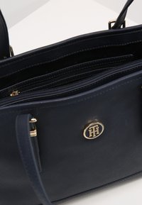 Sac à main en simili cuir marine avec quincaillerie dorée, plusieurs compartiments zippés et un accent logo à l'avant.