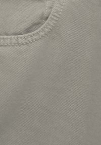 Gros plan sur un tissu beige avec des coutures visibles le long d'une couture courbe, montrant une texture textile détaillée.