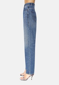 Jeans azules de tiro alto, lavado claro con un diseño de pierna recta. Presentan un bolsillo trasero, un ligero desvanecimiento y un dobladillo limpio. Combinados con sandalias de tacón metálico.
