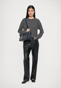 Zwart-wit gestreepte lange mouwen top, hoge taille zwarte leren broek, met een marineblauwe handtas met accenthardware, zwarte instapschoenen.