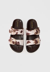 Σανδάλια με σχέδιο από καφέ και λευκό αγελάδας, με δύο ρυθμιζόμενες λωρίδες και χρυσές αγκράφες, διαθέτουν σκούρο καφέ μαλακό πέλμα.