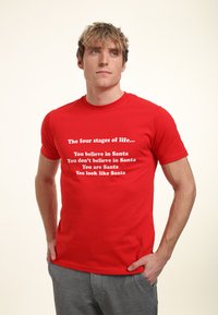Rød bomuld t-shirt med hvid tekst, der indeholder humoristiske sætninger om Santa, korte ærmer og rund halsudskæring. Teksten er arrangeret i fire linjer.